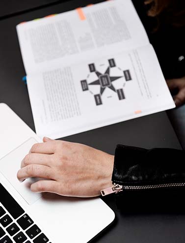 CBS studerendes hånd på en touchpad på en computer, åben bog ved siden af